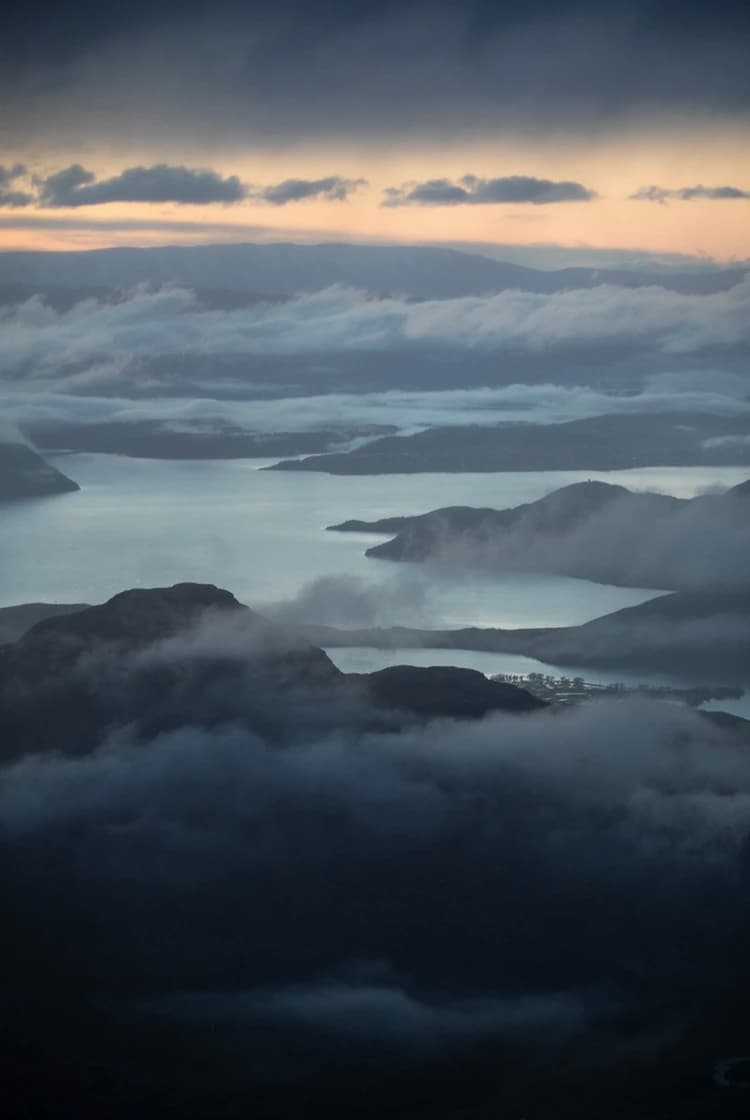 A stunning aerial view of mist-covered mountains and lakes at dusk, with layers of clouds gently floating over the water and peaks, creating a serene and mystical landscape.