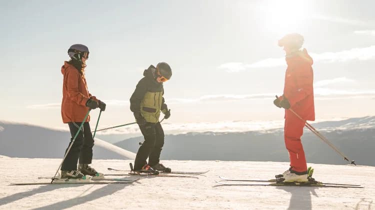 Two people taking a ski lesson at the top of Cardrona Alpine Resort, New Zealand, with instructors guiding them on snow-covered slopes and a panoramic view of surrounding mountains.