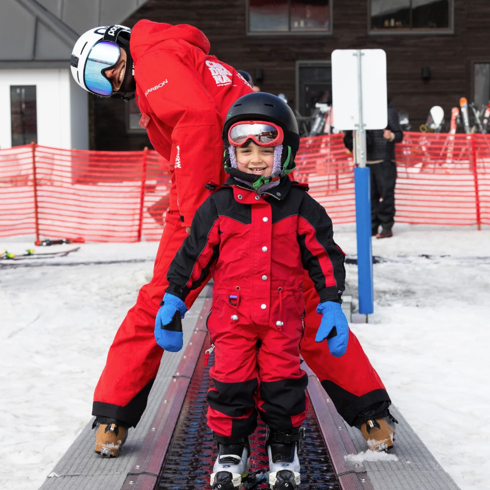 Young child in a red ski suit, smiling with ski instructor in the learner's conveyer belt at Cardrona Alpine Resort