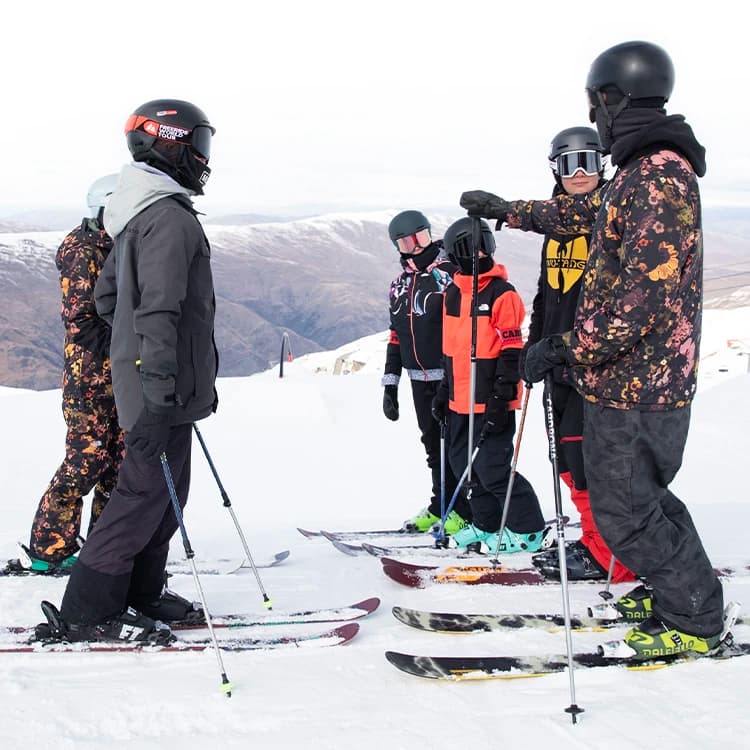 A group of skiers at Cardrona Alpine Resort listens attentively as an instructor points out the terrain, preparing them for an exciting day on the slopes.