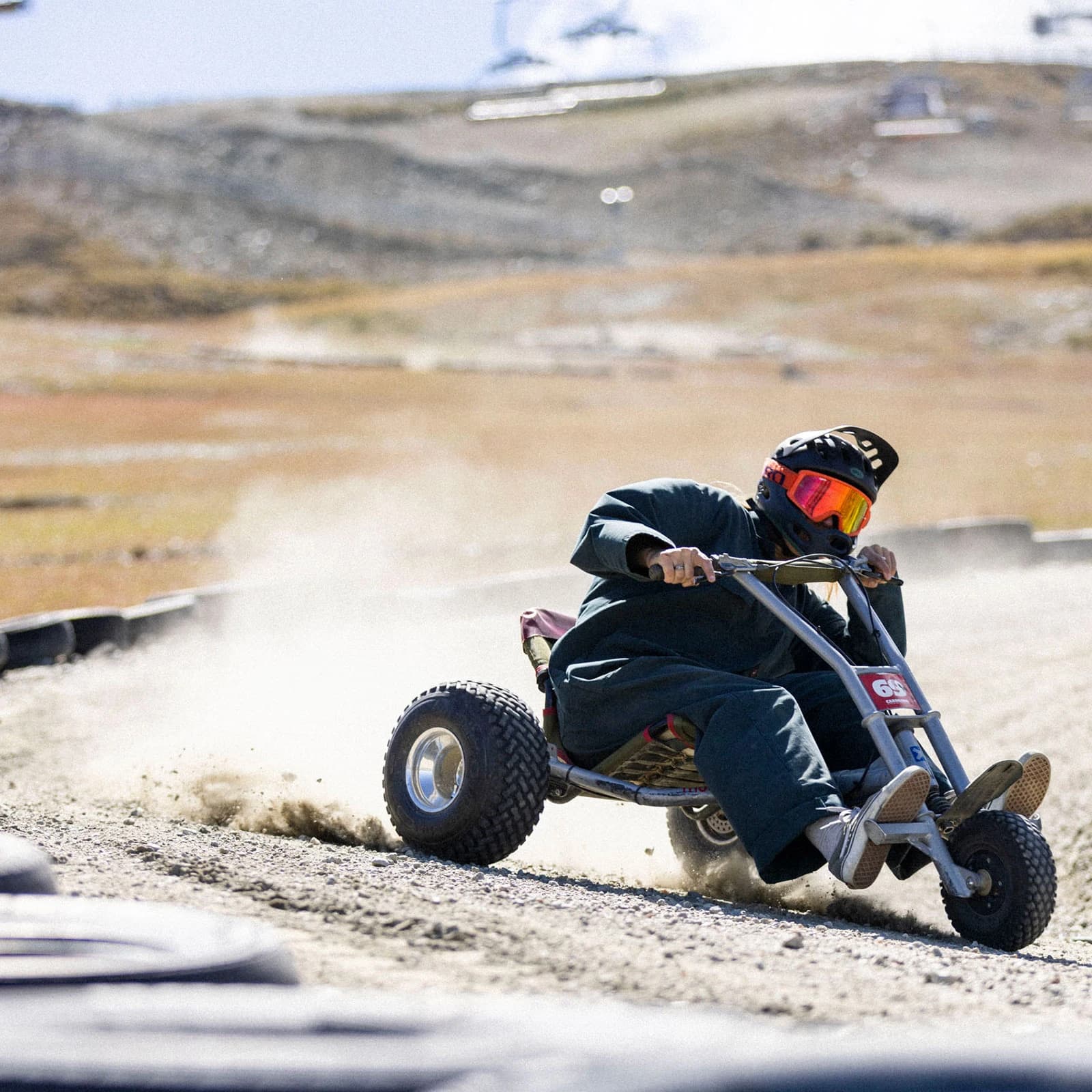 Rider mountain carting at Cardrona Alpine Resort. Rider is wearing dark green suit and full-face helmet, navigating a corner, with dust in the background. 