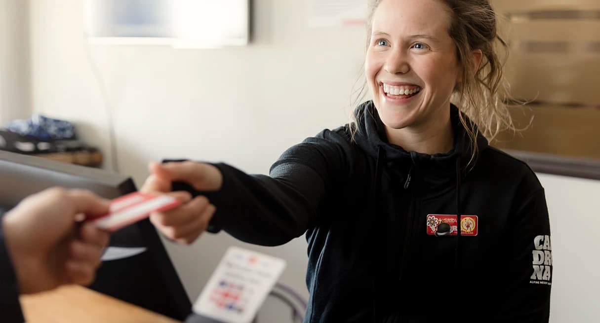 A smiling staff member hands across a lift pass to a customer.