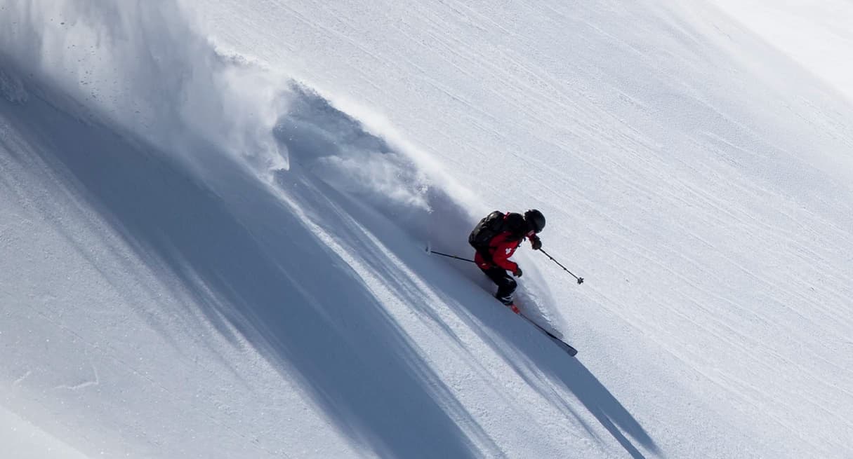 A ski patroller creates a trail of snow as they descend a ski run.