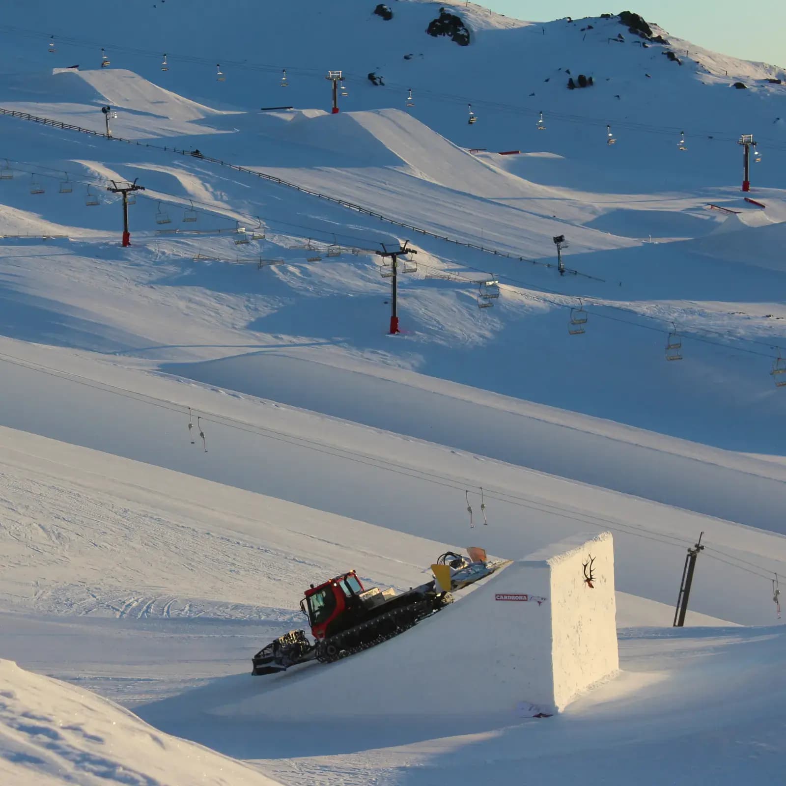 Tom Campbell in a snow groomer on the Big Air jump at sunrise. 