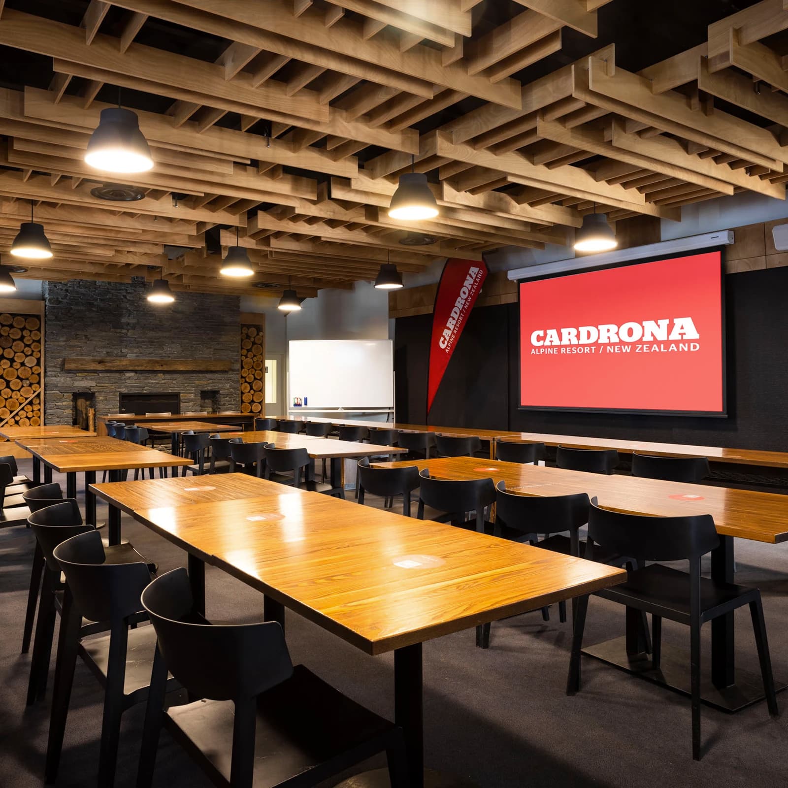 An empty conference room with tables and chairs set up looking on to a large screen branded with "Cardrona". 