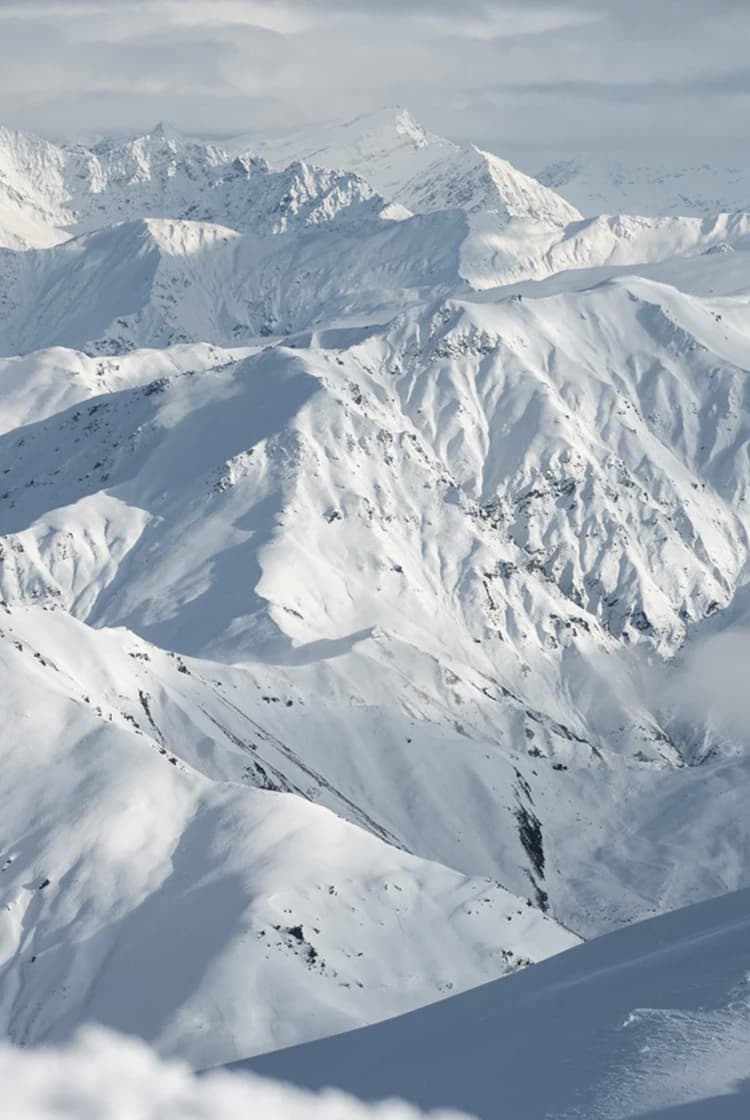 A breathtaking view of the snow-covered mountain ranges of Treble Cone, showcasing the expansive terrain and steep alpine features, perfect for skiing and snowboarding enthusiasts.