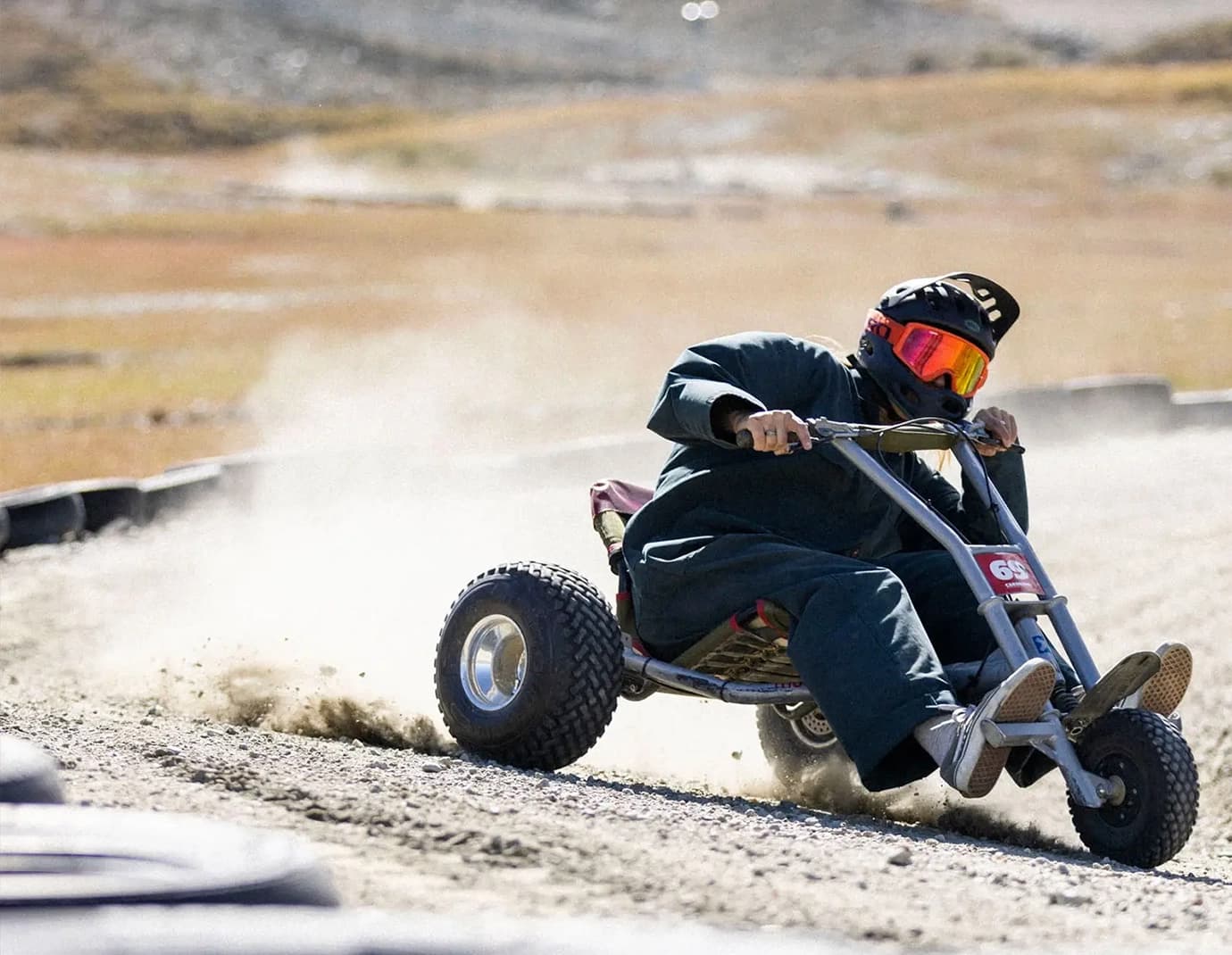 A person riding a mountain cart, creating a trail of dust on a gravel track.