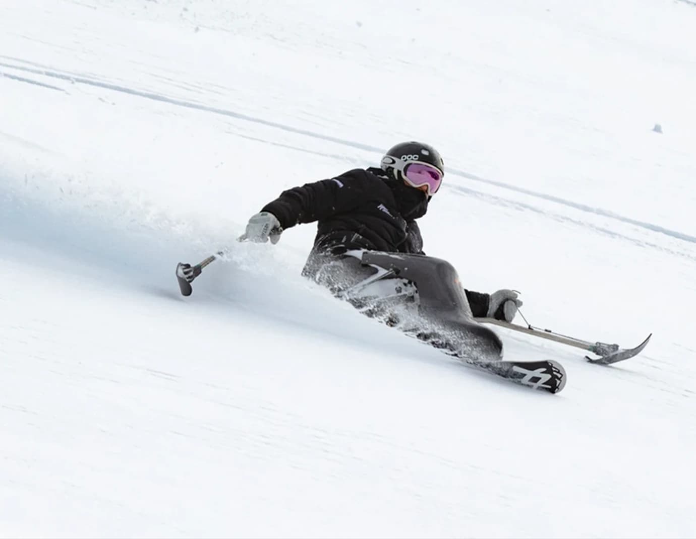 A skier in adaptive equipment carves through fresh snow at Treble Cone Ski Field, leaving a trail of powder on the steep, snowy slope.