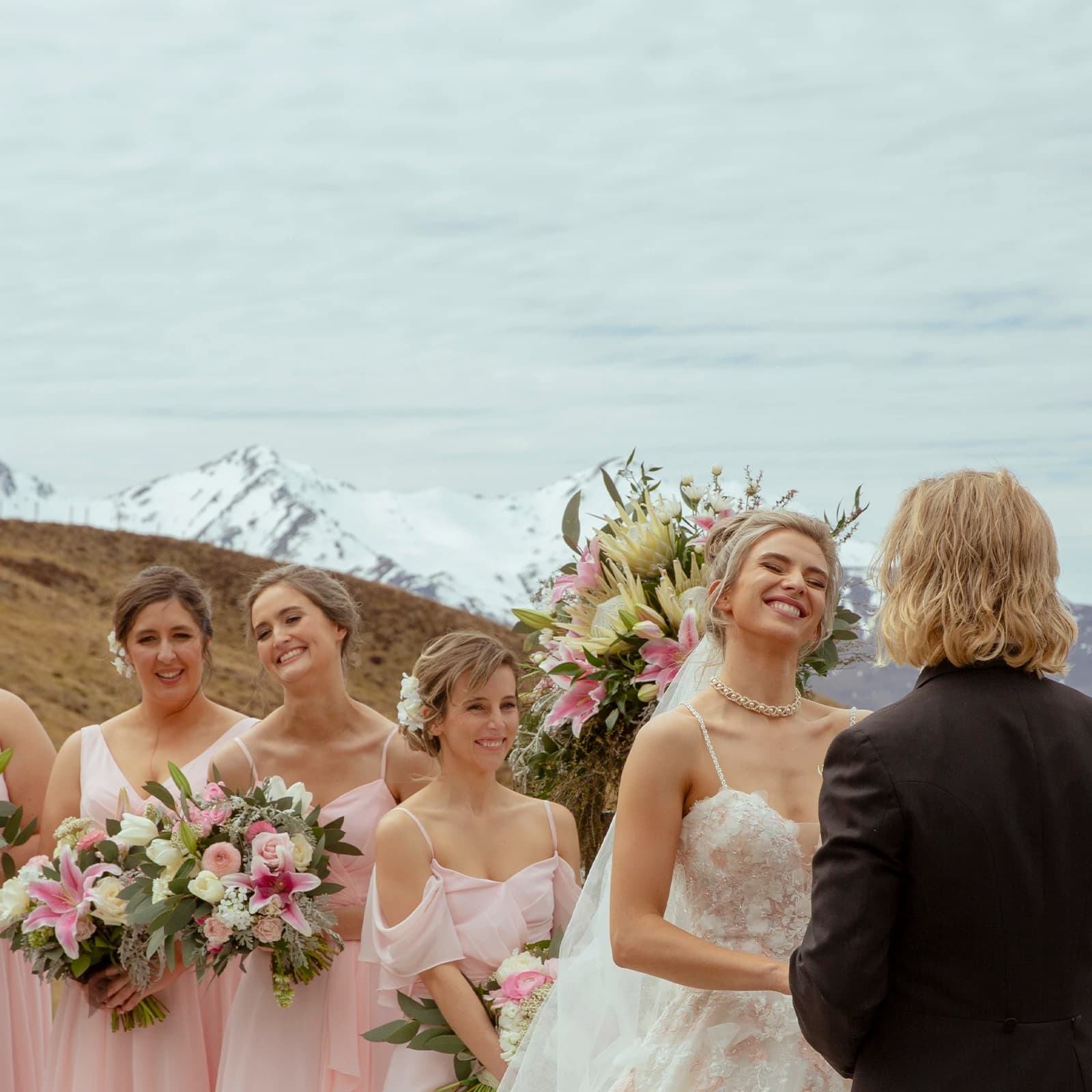 A bride, groom and four bridesmaids stand at the alter outside with snow-covered mountains in the background. 