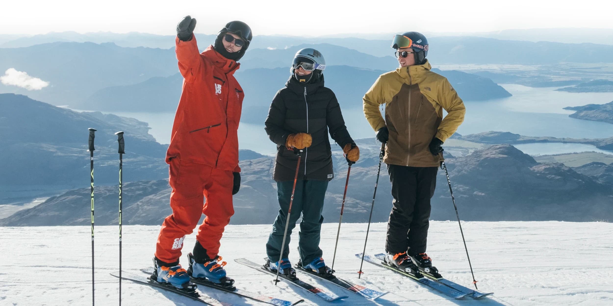 Two people taking a ski lesson at Treble Cone Ski Field, New Zealand, with instructors guiding them on snow-covered slopes and a panoramic view of surrounding mountains.