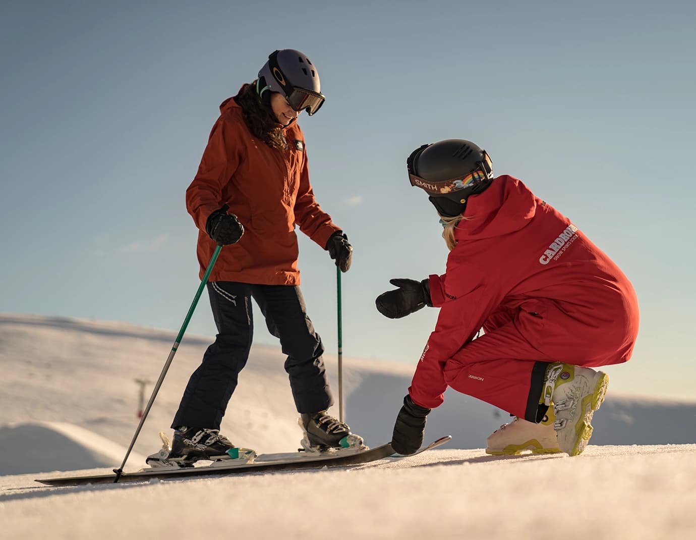 A ski instructor in red guiding a skier on a sunny slope.