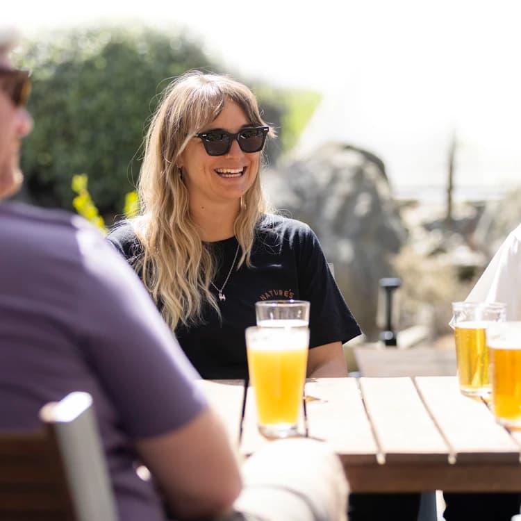 A group of four friends enjoy some beers at an outside table on a sunny day.