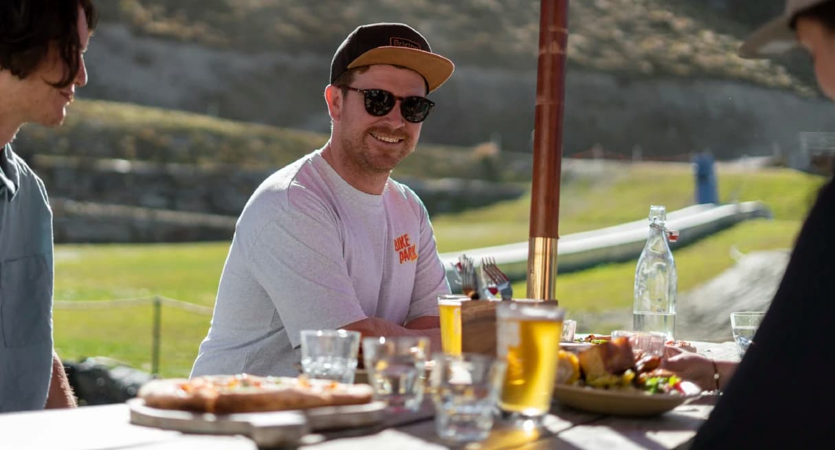 A man sits down with friends and enjoys a beer and pizza in the sunshine.