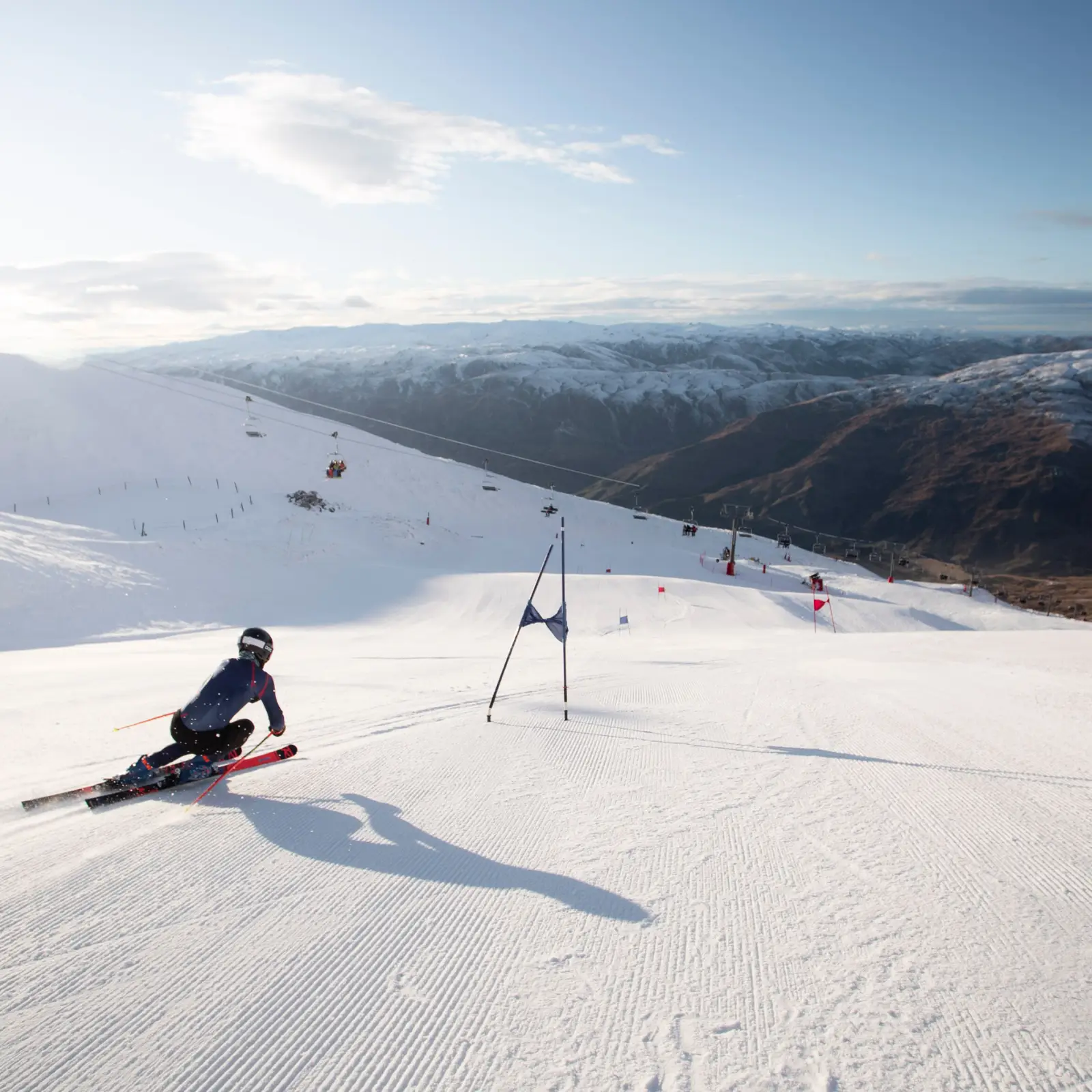 Alpine skier racing down a wide groomed slope with mountain views.