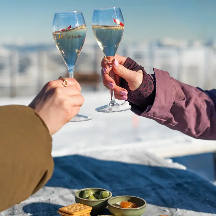 Two people clinking glasses of sparkling wine against a snowy mountain backdrop.