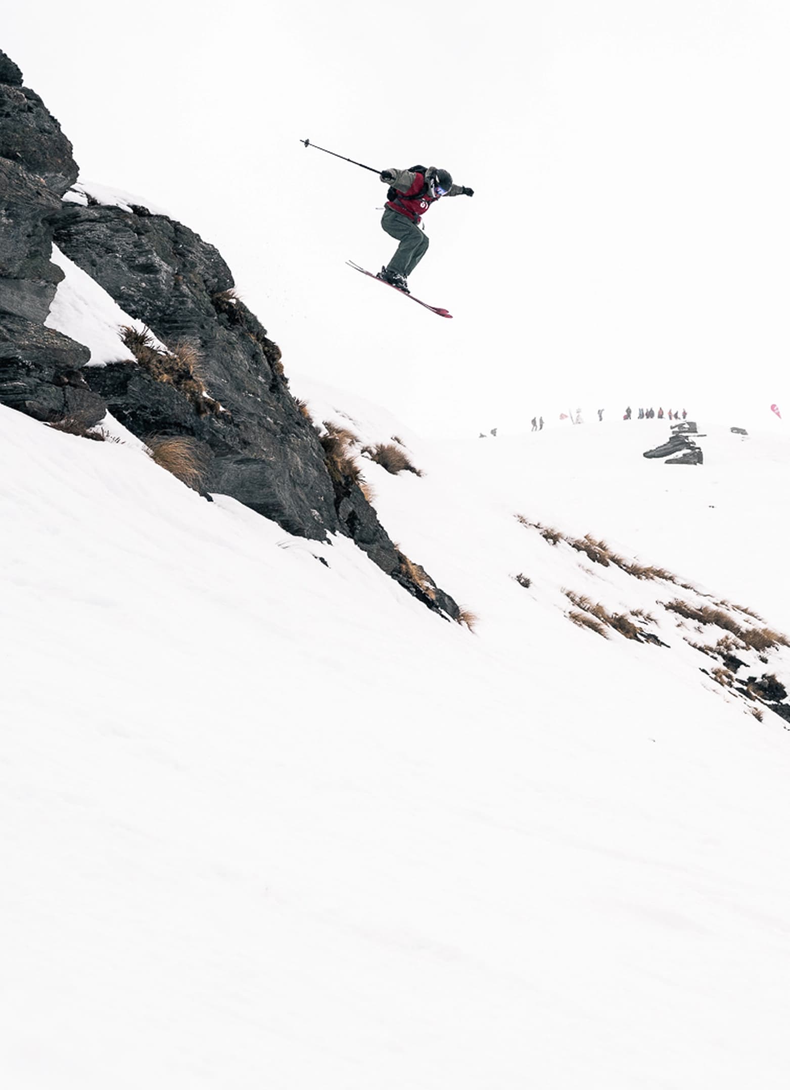 Junior skier dropping off a rocky cliff in a big mountain freeride competition.