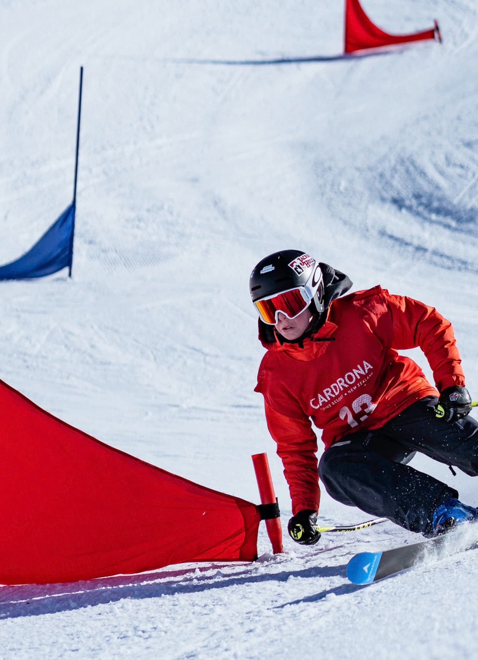 A focused young skier in a Cardrona race bib carves tight around a slalom flag.