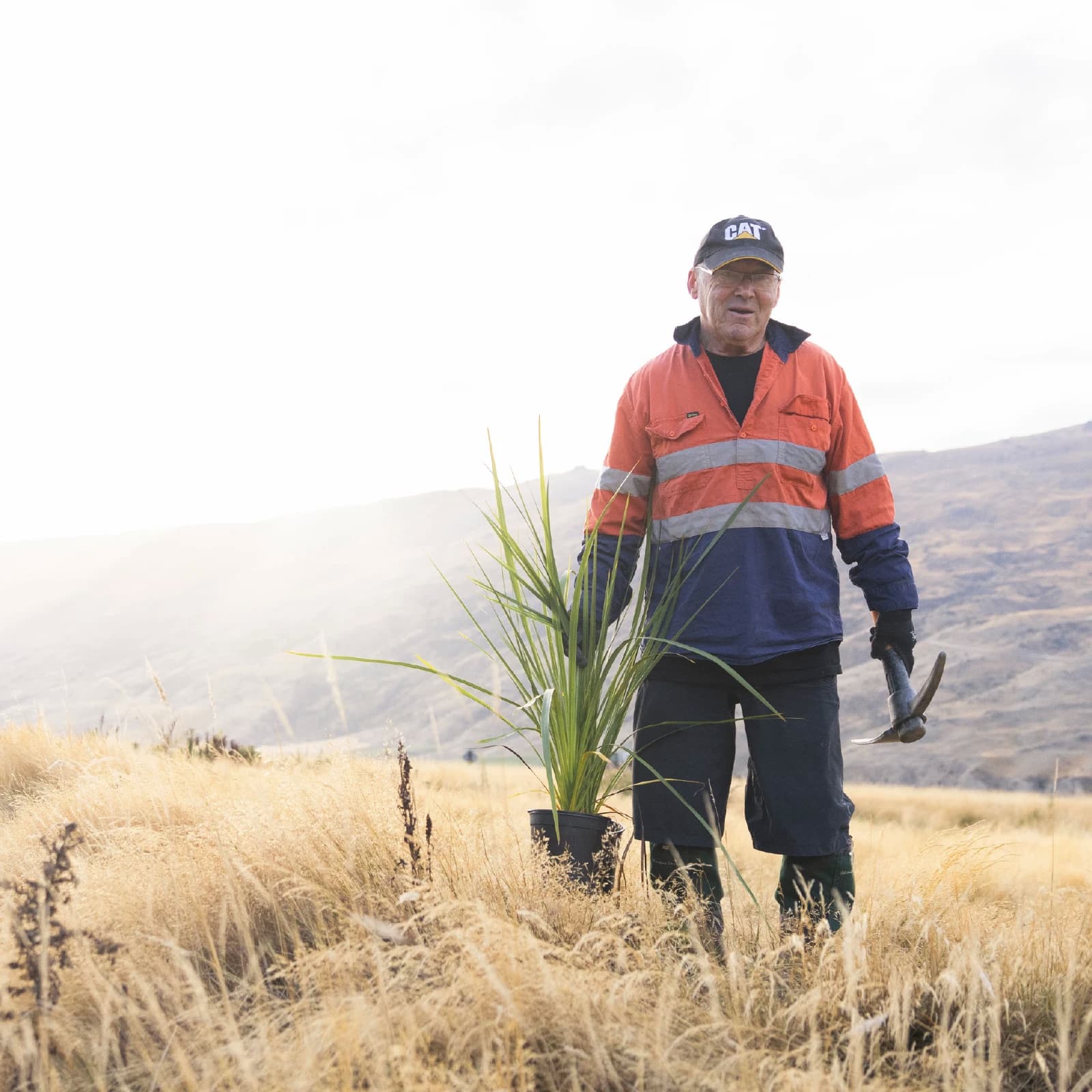 Man in high visibility vest holding a native New Zealand plant and tool, ready to plant at Cardrona Alpine Resort