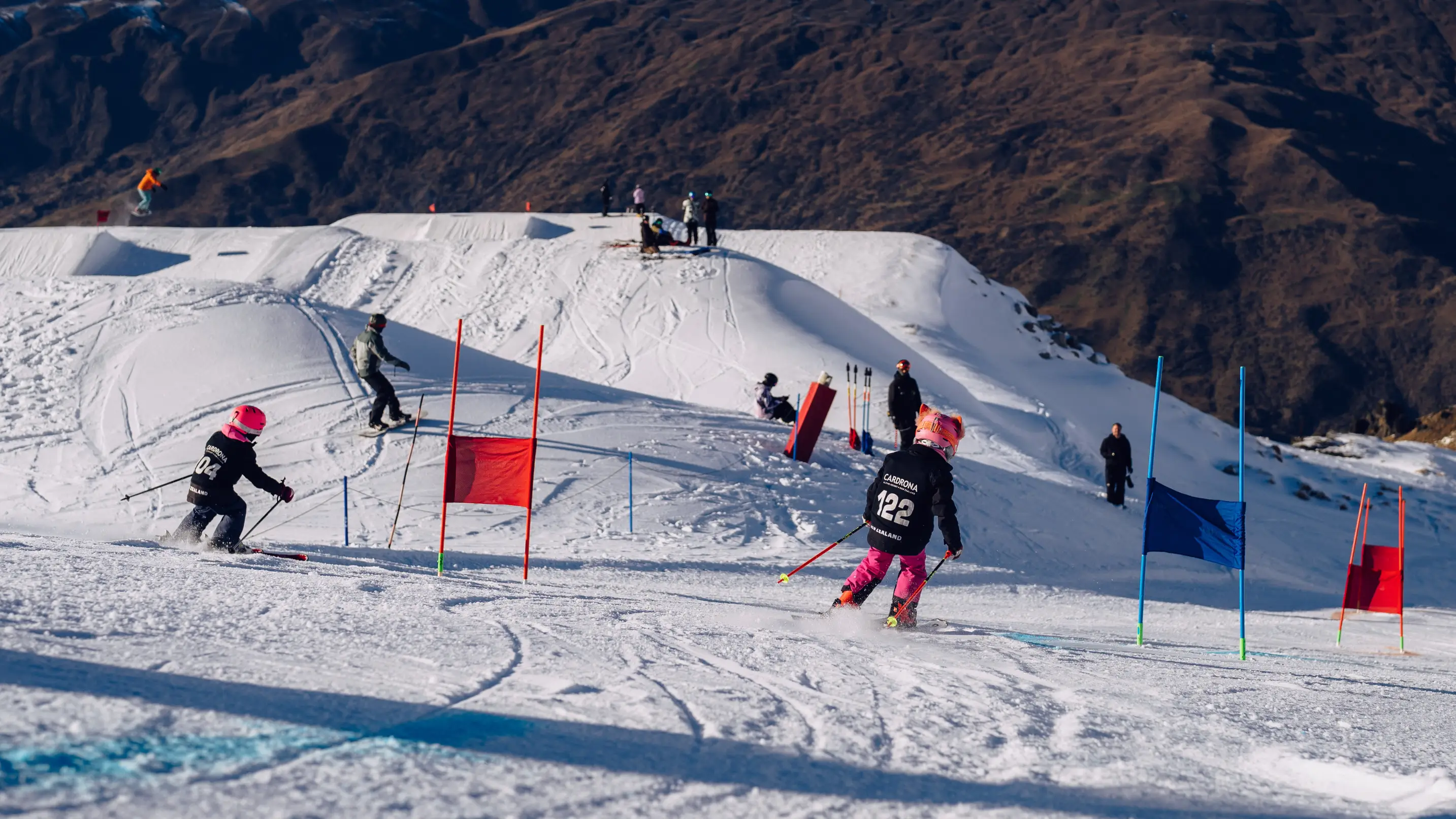Two young child racers in Cardrona bibs navigating a slalom course with red and blue gates.