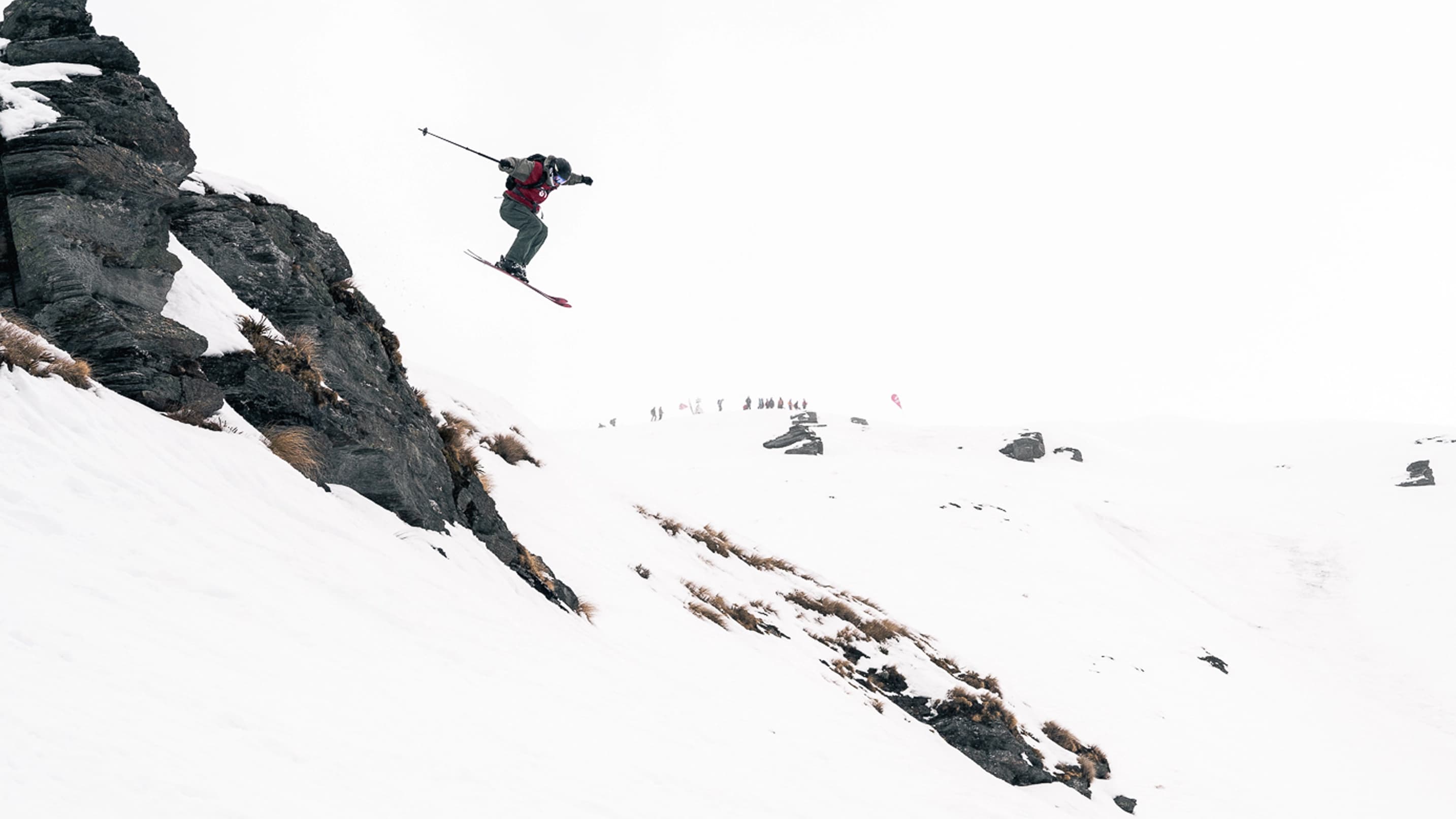 Junior skier dropping off a rocky cliff in a big mountain freeride competition.