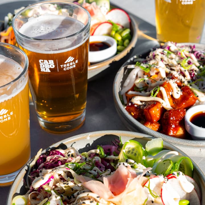 Cardrona and Treble Cone branded pint glasses of beer beside two bowls of Asian-style salads and toppings.