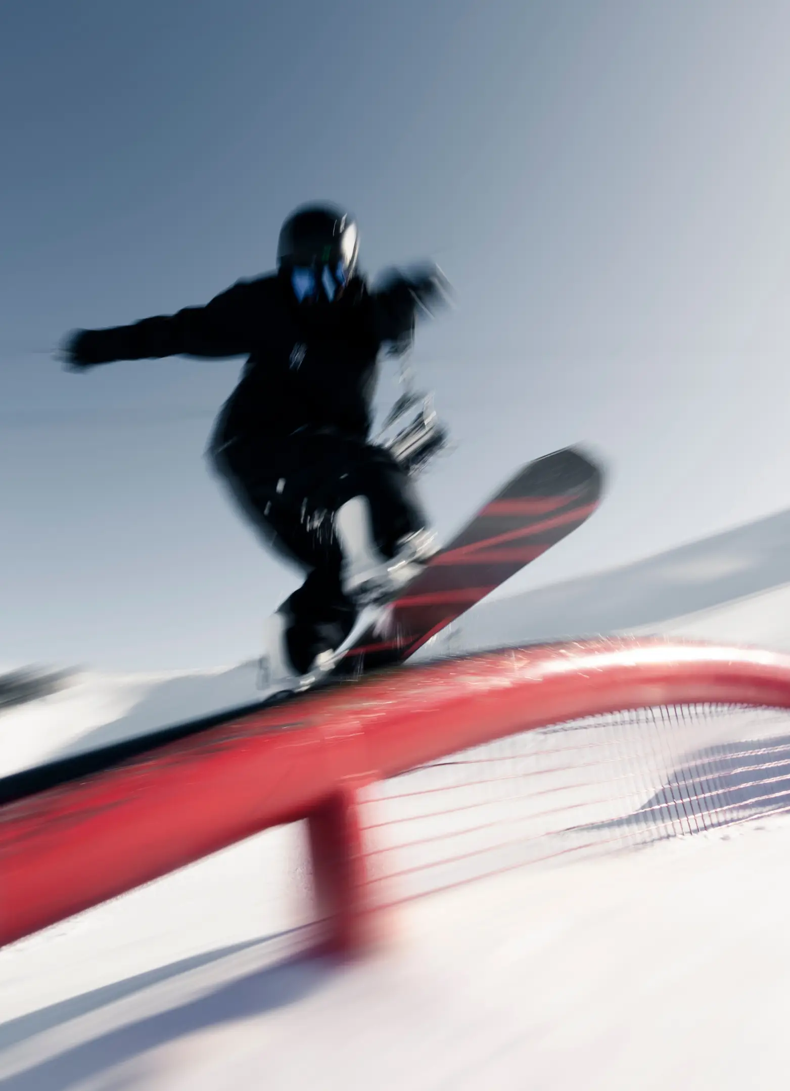 Snowboarder performing a trick on a red rail at a snowy terrain park.