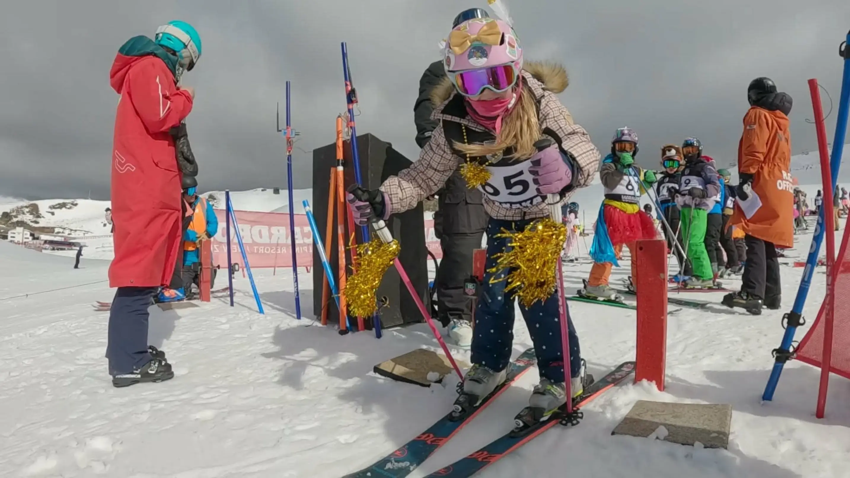 A young child gets ready to start a ski race, dressed up with gold tinsel.