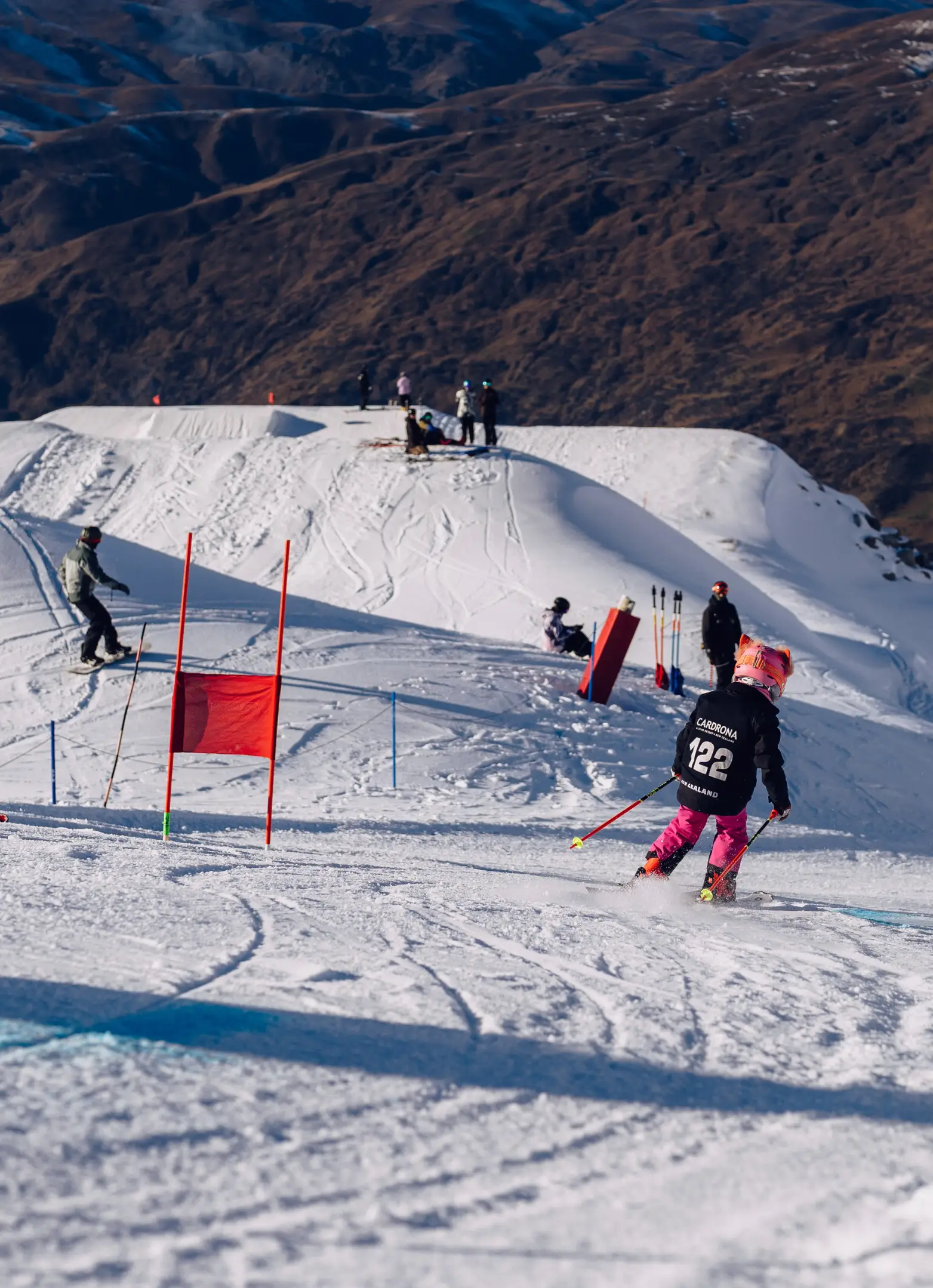 Two young child racers in Cardrona bibs navigating a slalom course with red and blue gates.