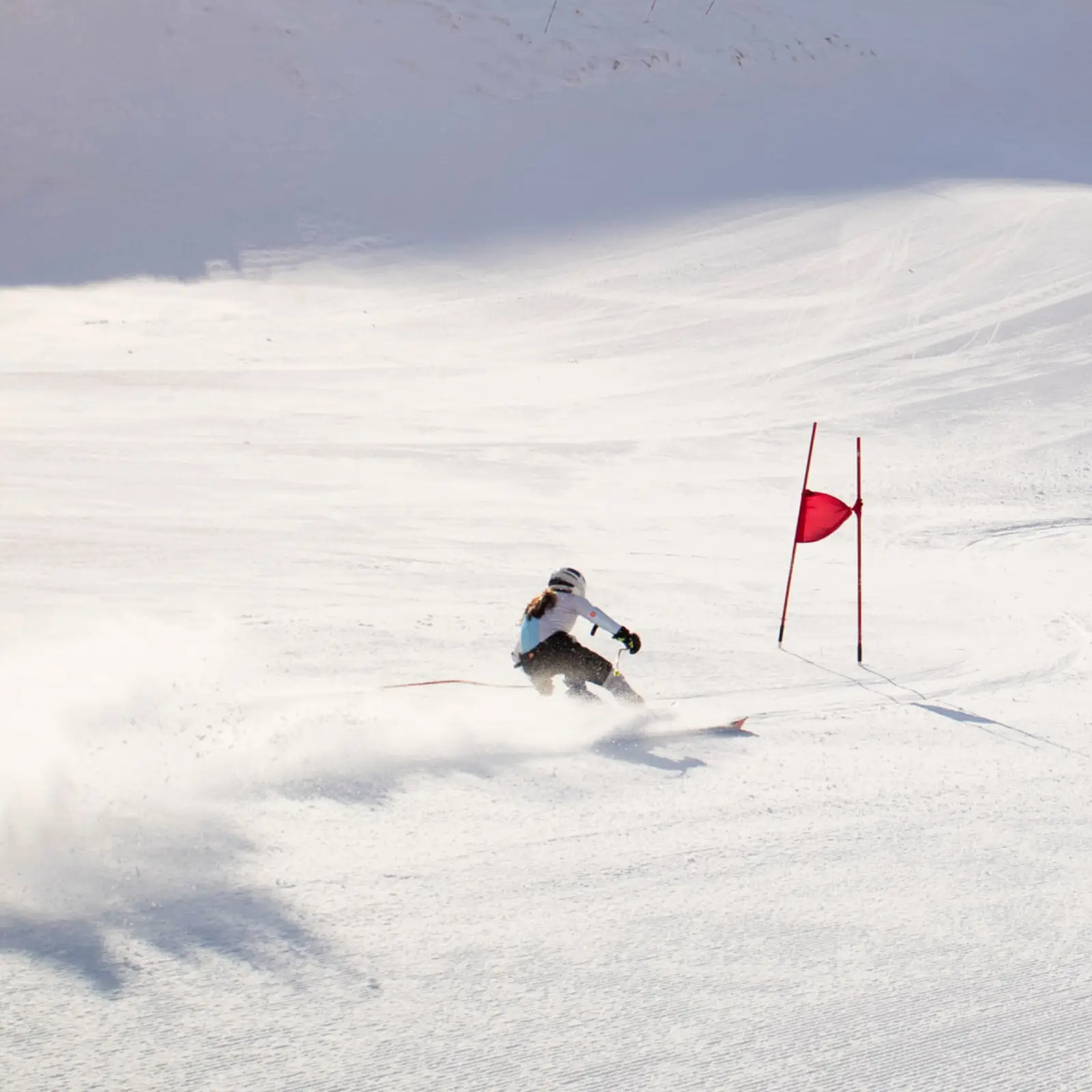 Skier carving around a red gate on a groomed race course.