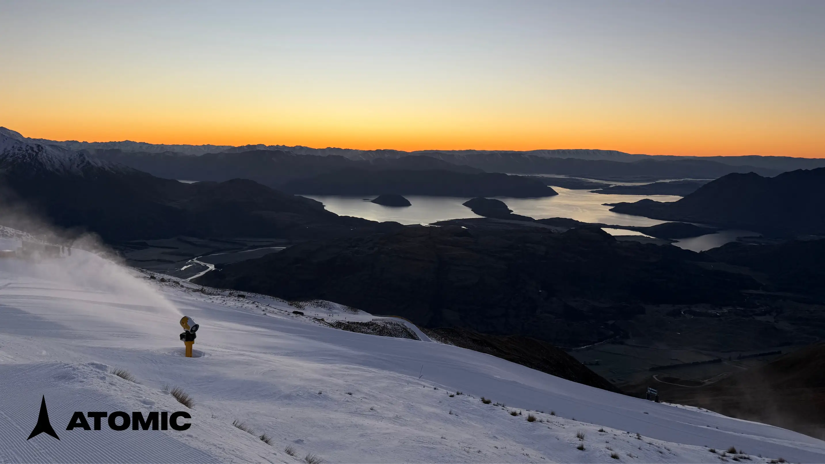 View of sunrise over a lake from a snowy mountain with Atomic logo in the corner.