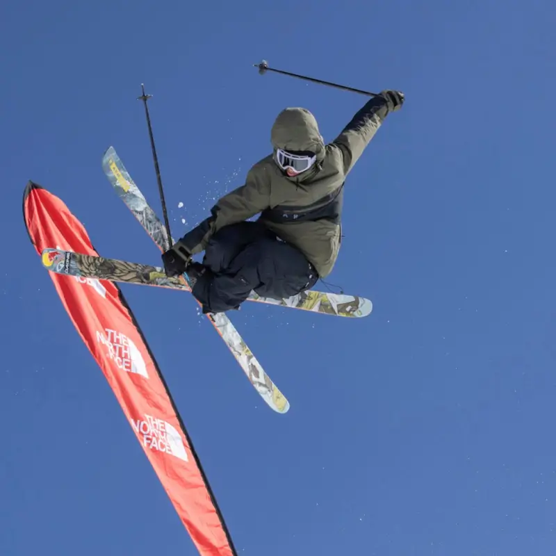 Skier does a high jump against a bright blue sky and The North Face teardrop flag.