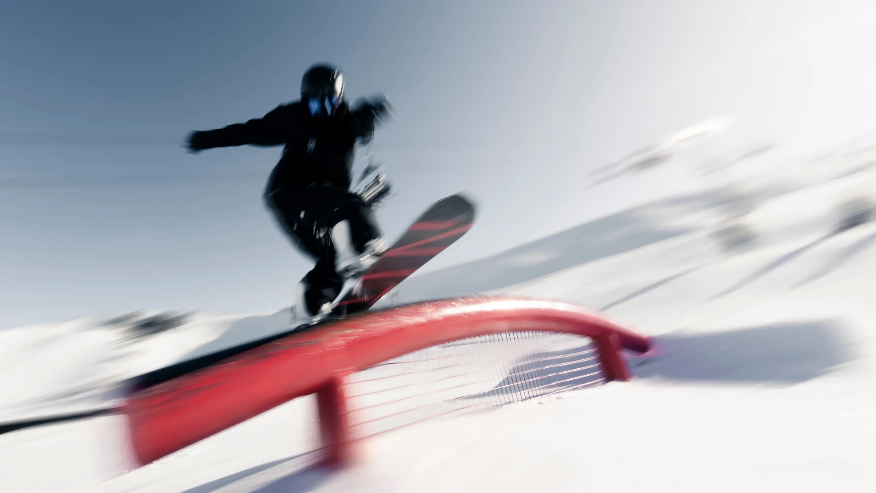 Snowboarder performing a trick on a red rail at a snowy terrain park.
