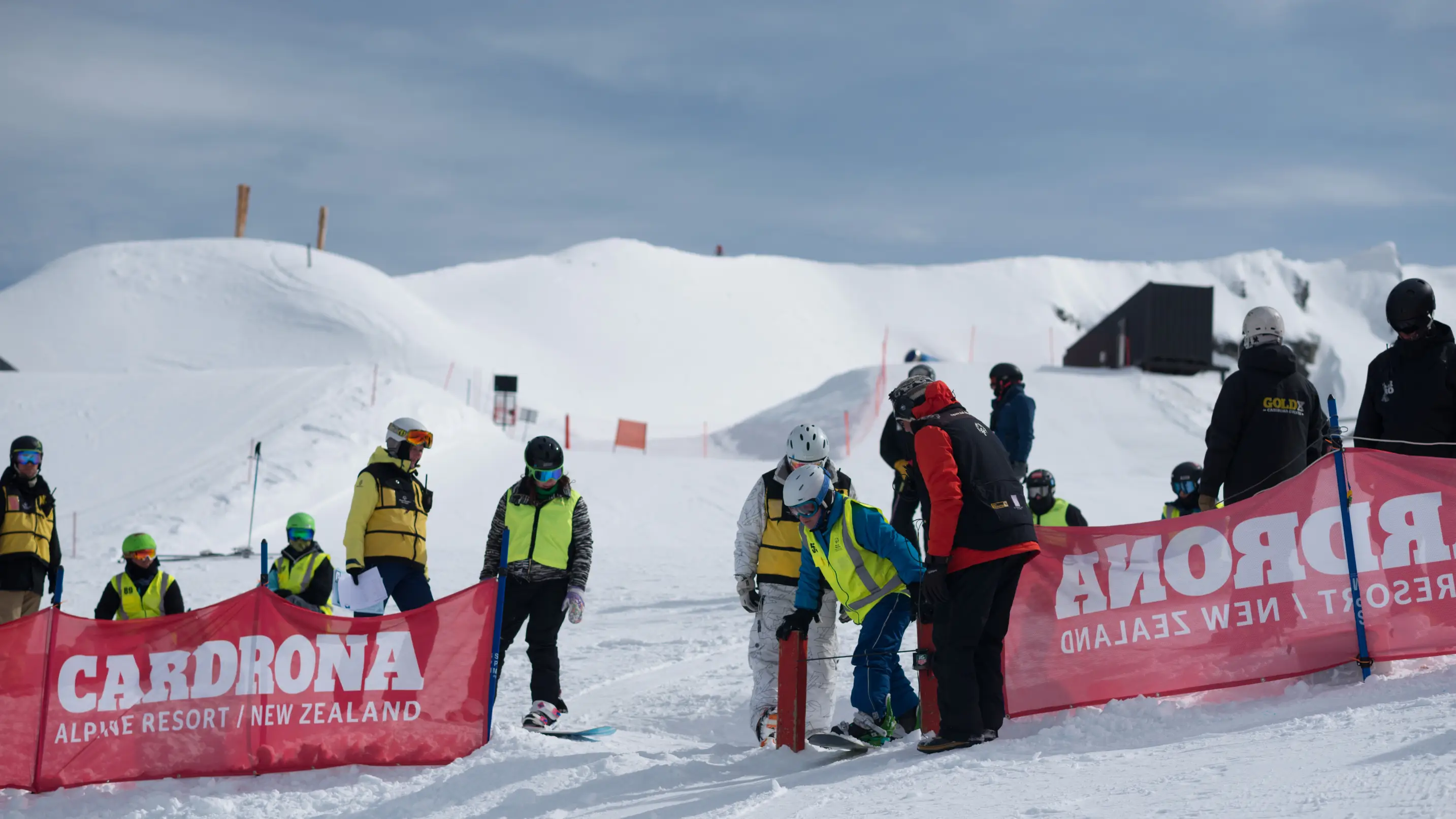A snowboarder being assisted through the start gate by volunteers in hi-vis vests at Cardrona Alpine Resort.