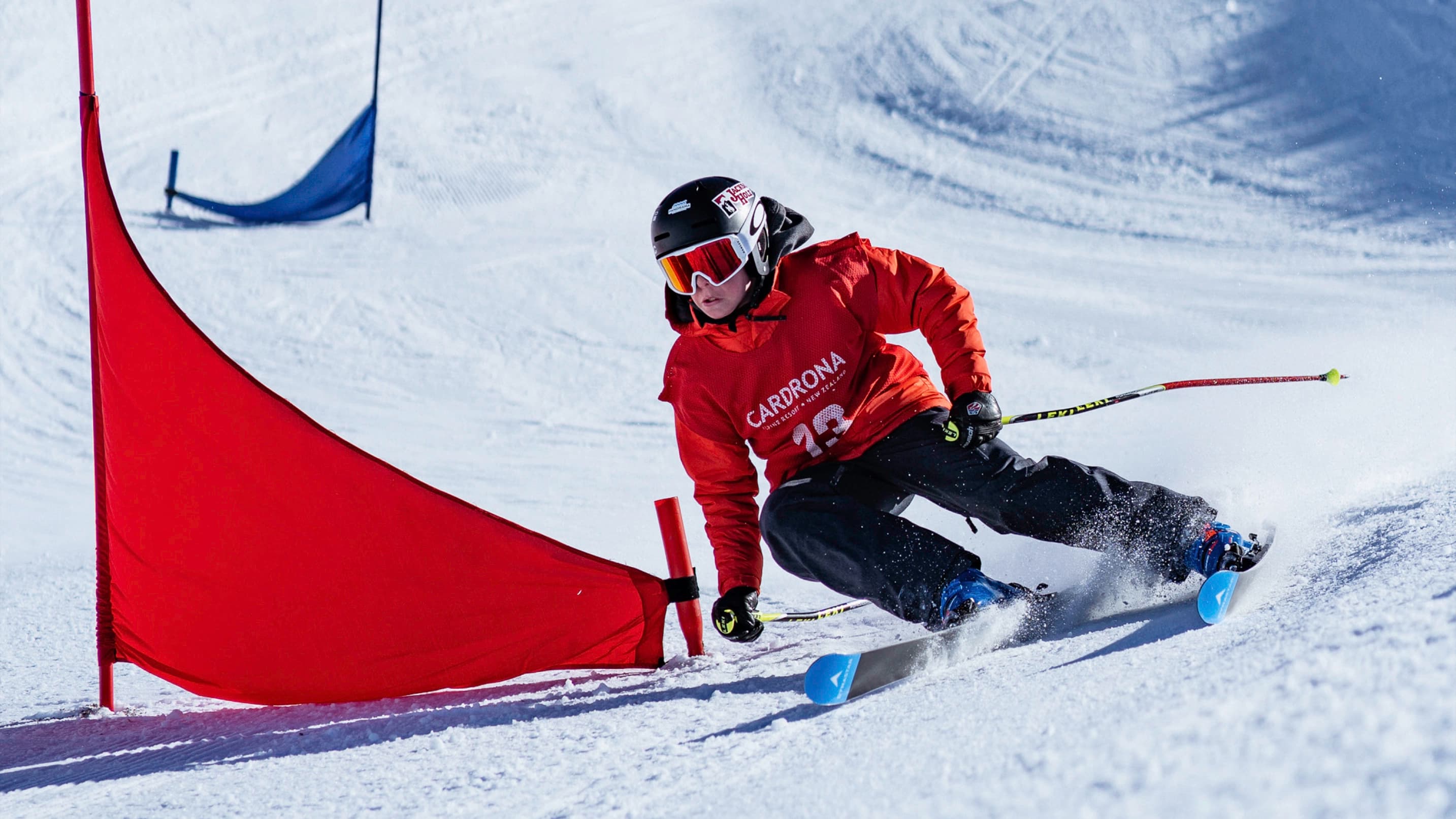 A focused young skier in a Cardrona race bib carves tight around a slalom flag.