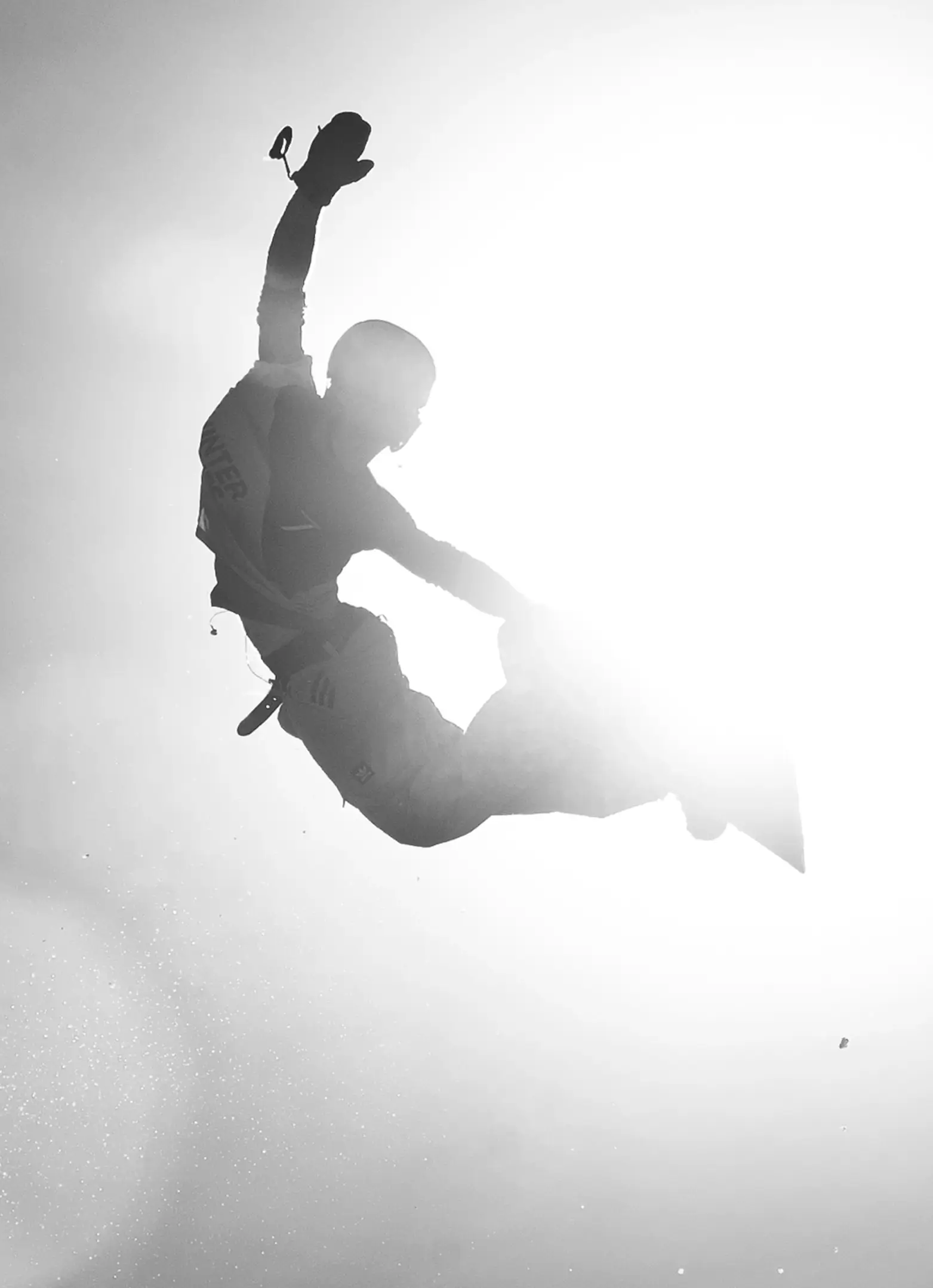 Silhouette of a snowboarder mid-air performing a grab trick against a bright sunlit sky, showcasing dynamic movement and freestyle energy.
