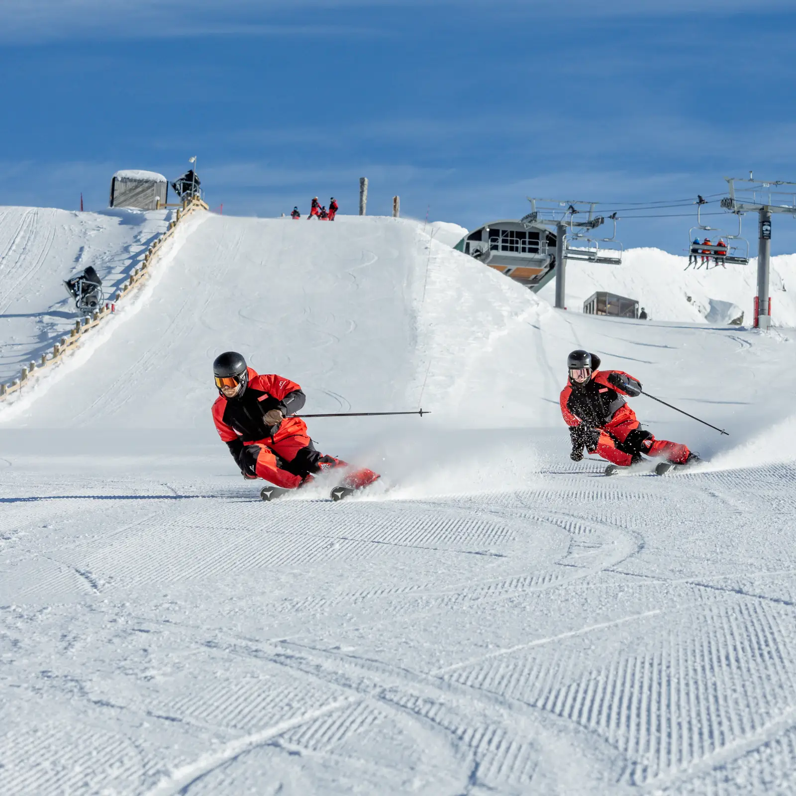 Two skiers carve down Cardrona in ITC red uniforms.