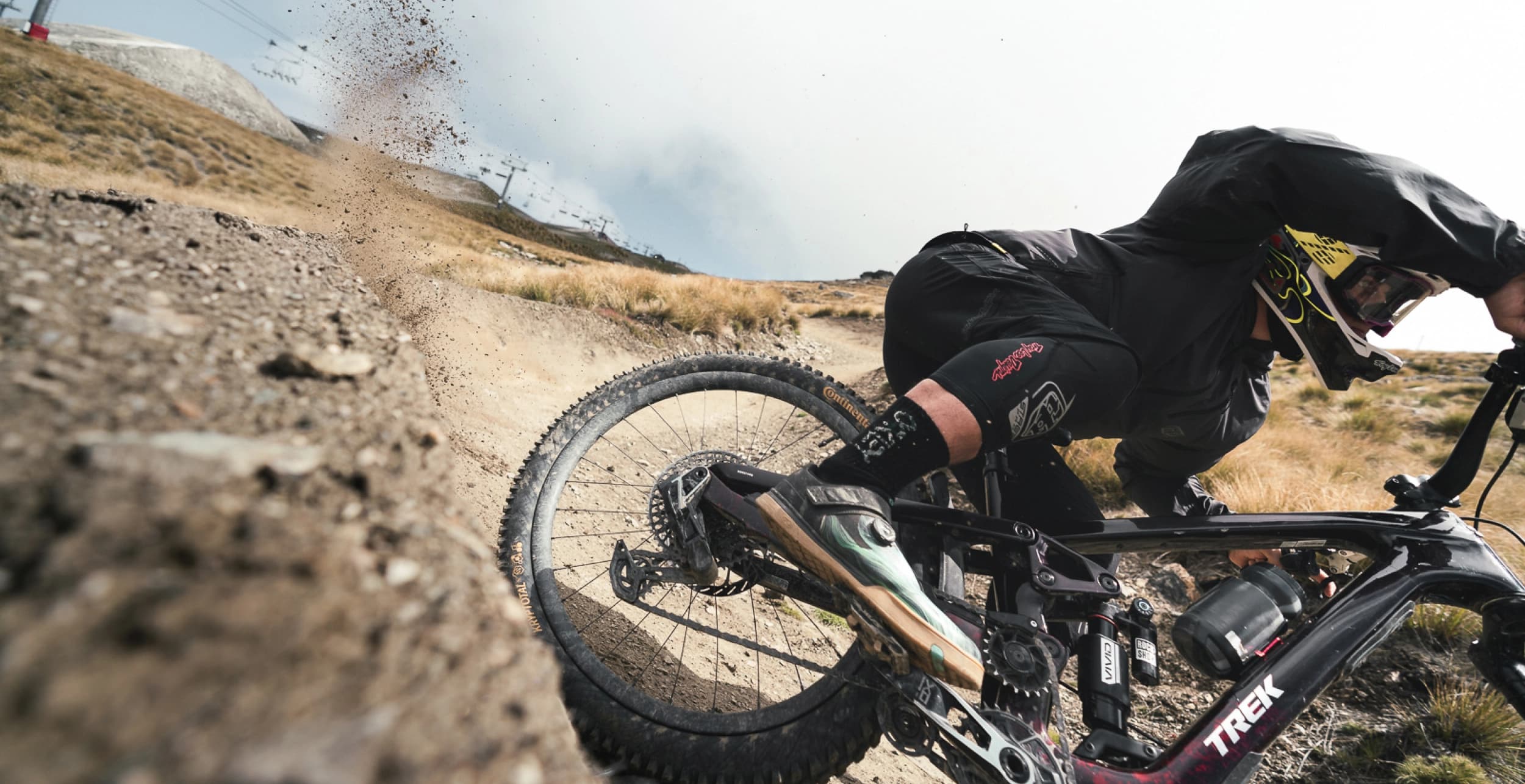 A mountain biker carving through a dirt berm at speed, leaning low as gravel sprays from the rear tire.