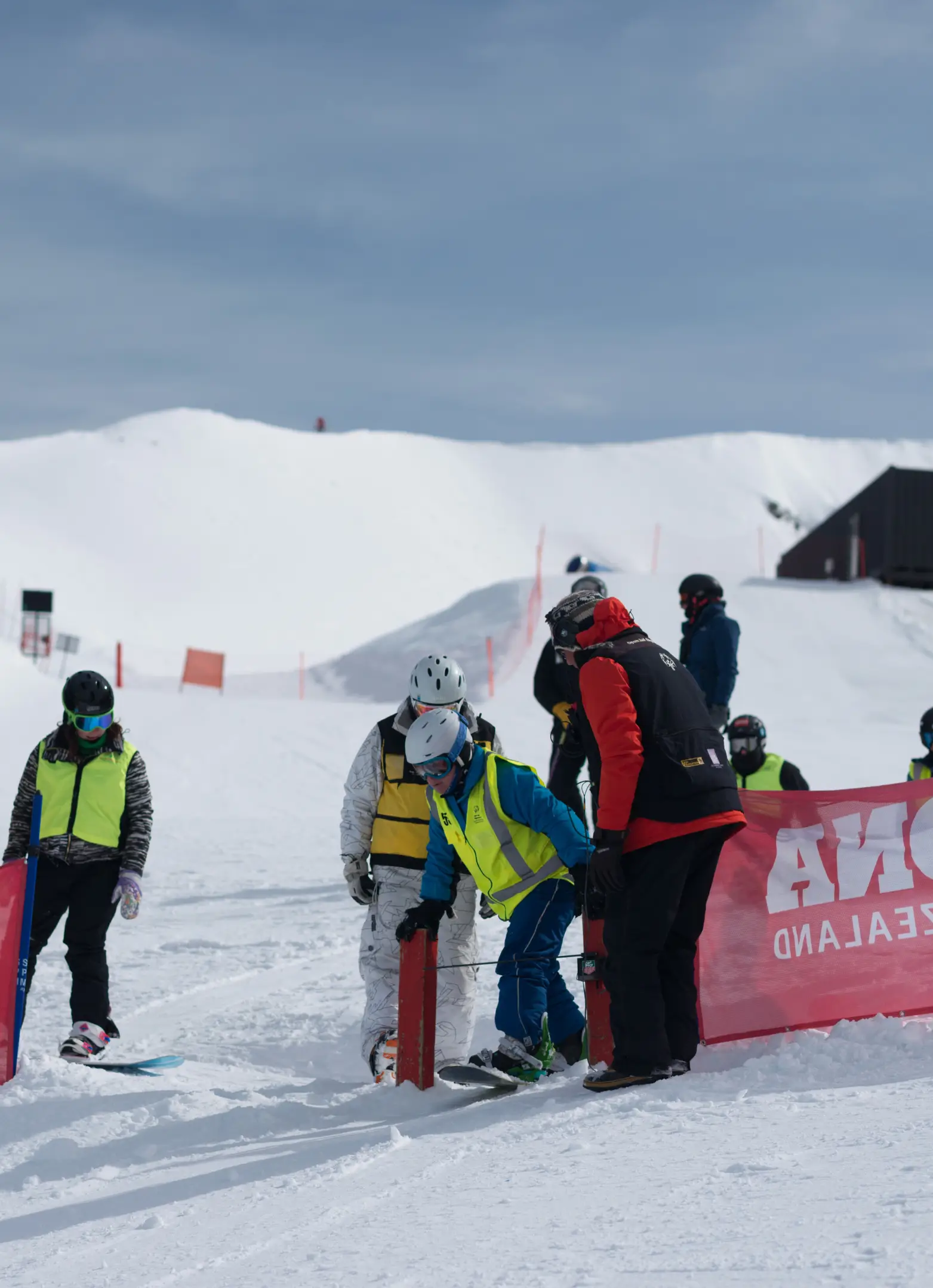 A snowboarder being assisted through the start gate by volunteers in hi-vis vests at Cardrona Alpine Resort.