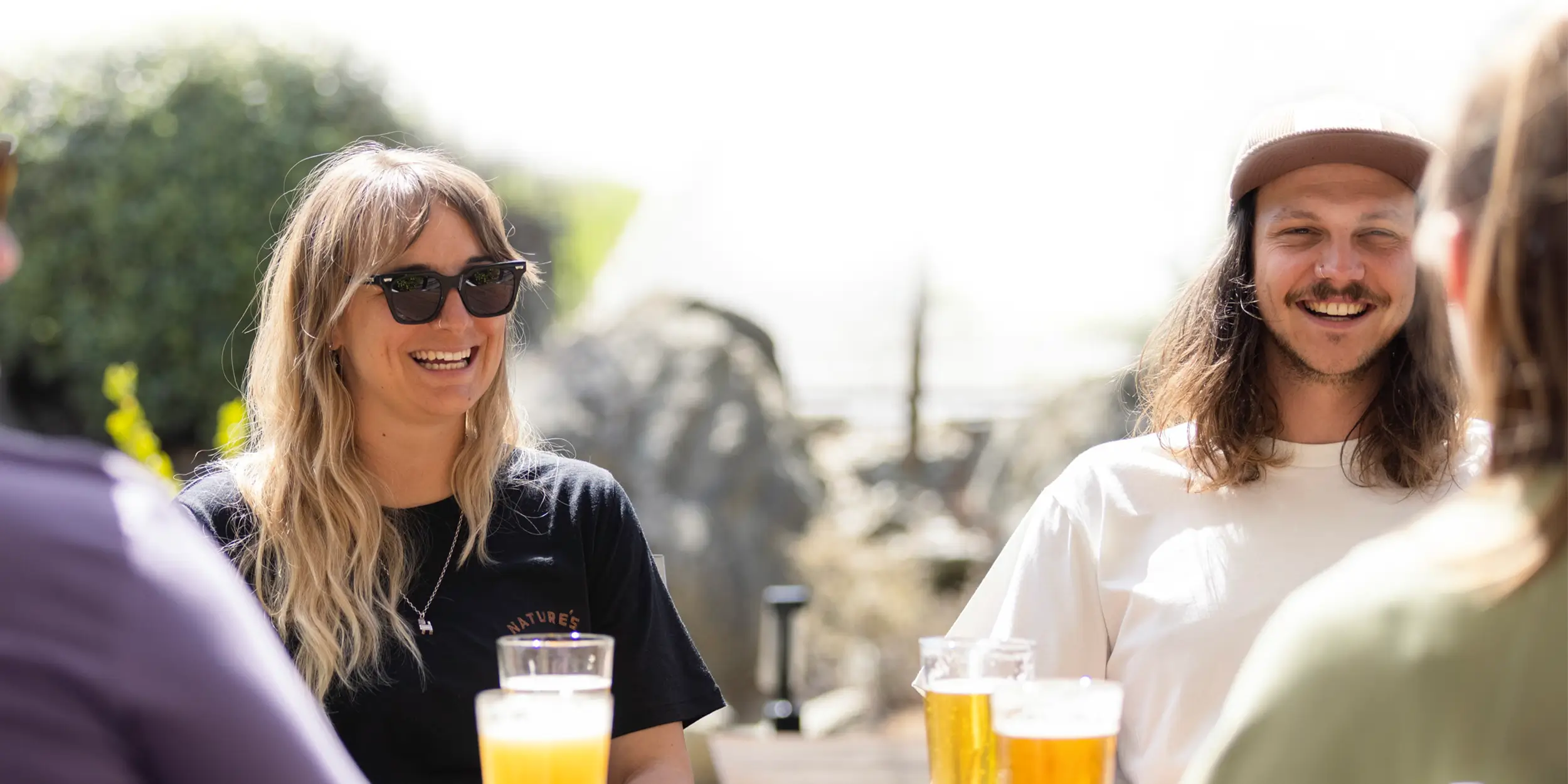 A group of four friends enjoy some beers at an outside table on a sunny day.