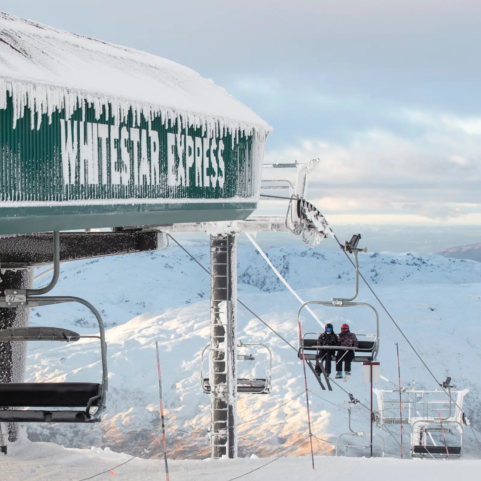 Frost-covered ski lift labeled “Whitestar Express” with riders ascending a snowy mountain.