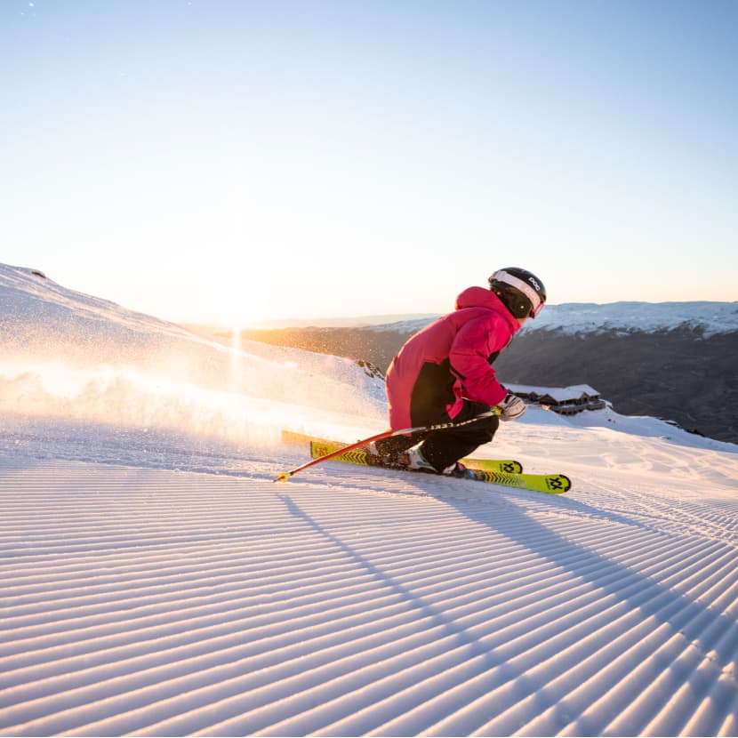 Skier carving down a groomed run at Cardrona Alpine Resort on a blue skies morning.