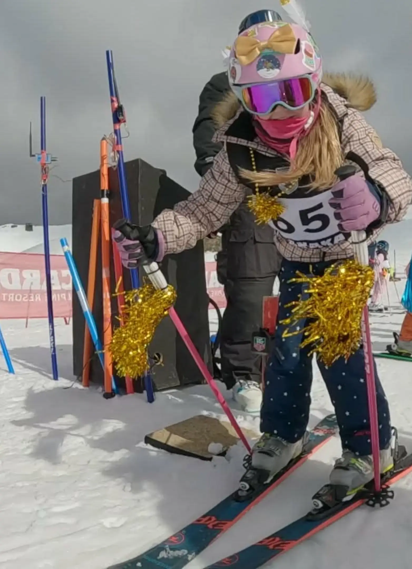 A young child gets ready to start a ski race, dressed up with gold tinsel.