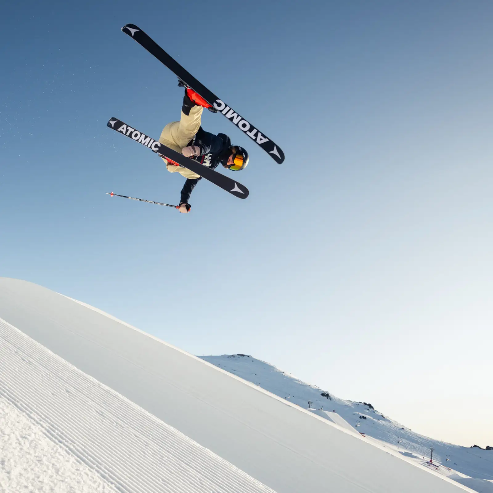 Skier with Atomic branded skis does a jump on a blue sky day.