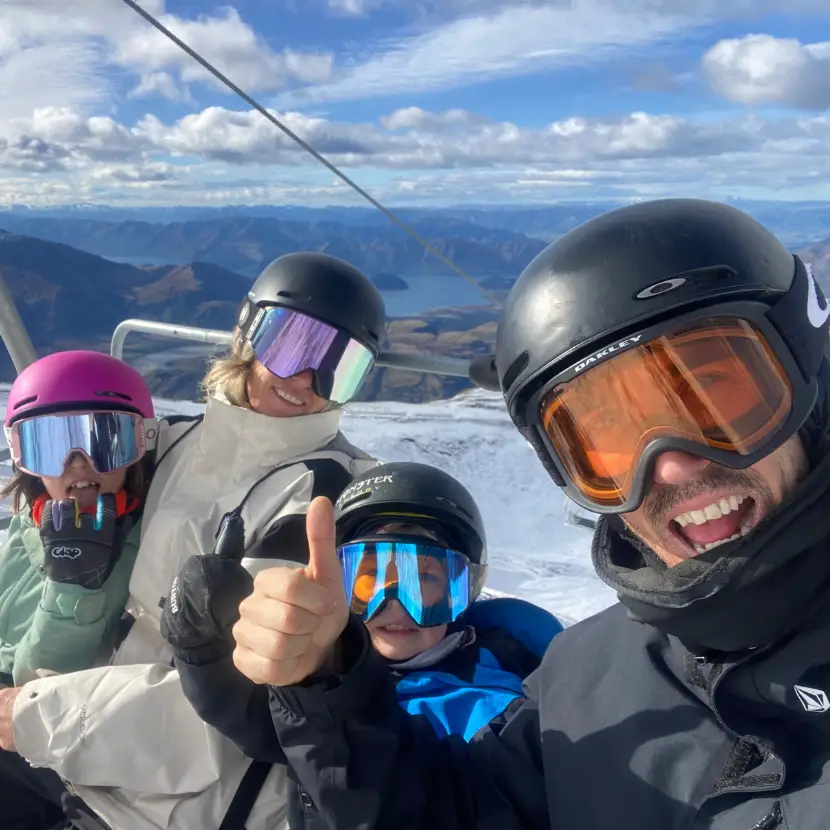 Selfie of a family of skies or snowboarders on a chairlift on a snowy mountain.