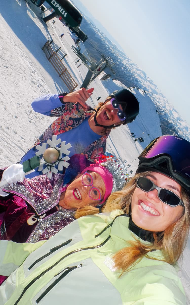 A group of skiers take an excited selfie on a sunny day on the mountain.