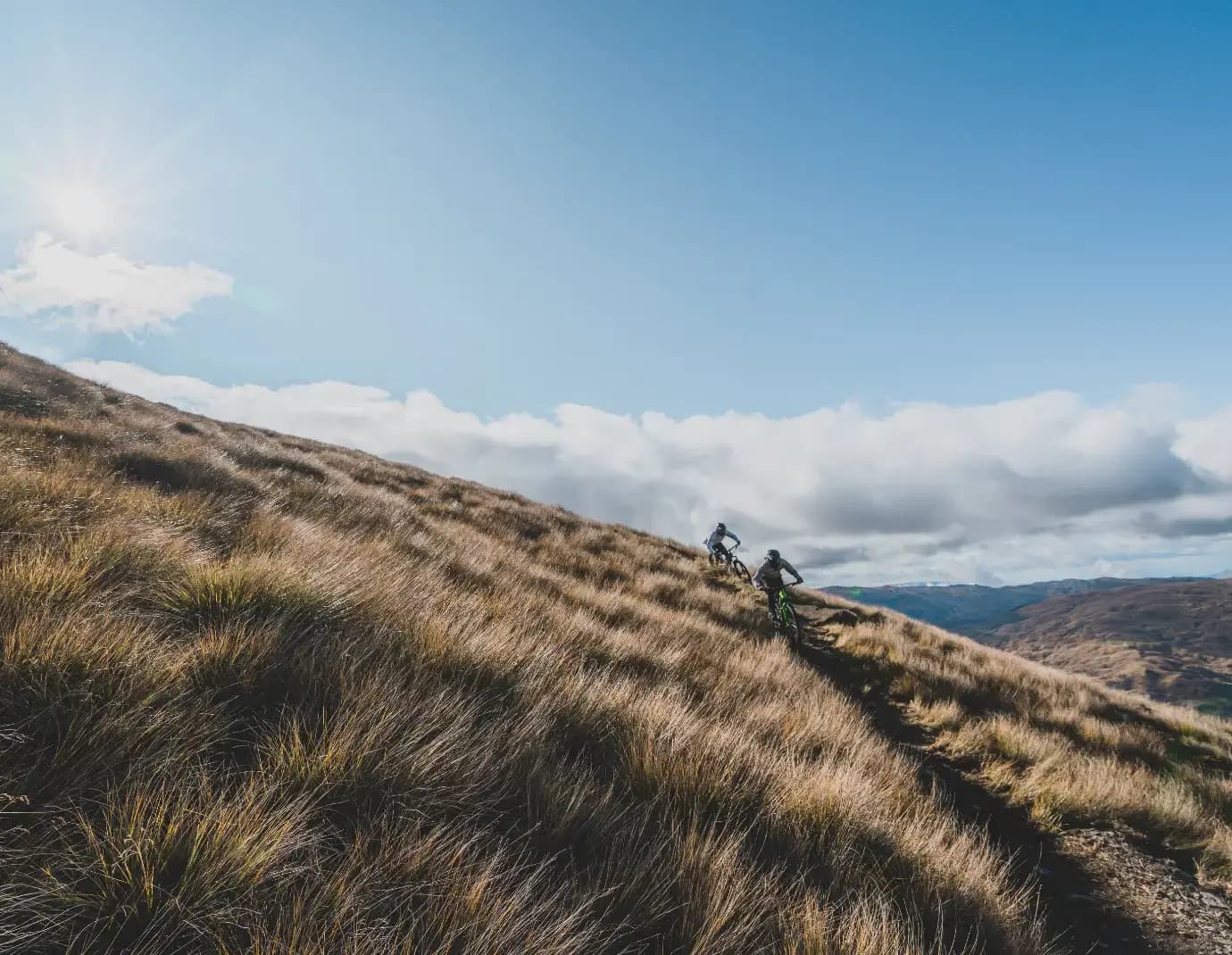 Two mountain bikers ride down a track on a blue sky summers day wearing t-shirts and full head helmets.
