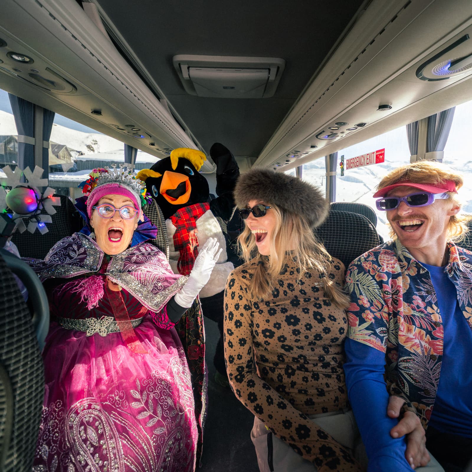 Two skiers, a penguin mascot and fairy god mother sit on the ski bus.