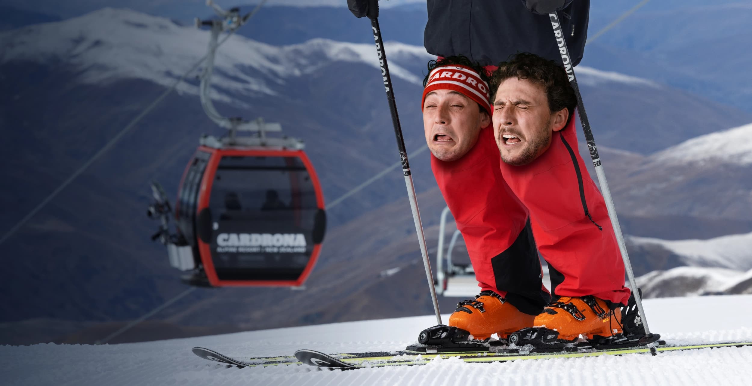 Two skiers in a novelty two-headed costume skiing on a groomed slope with a Cardrona gondola and mountain scenery in the background.