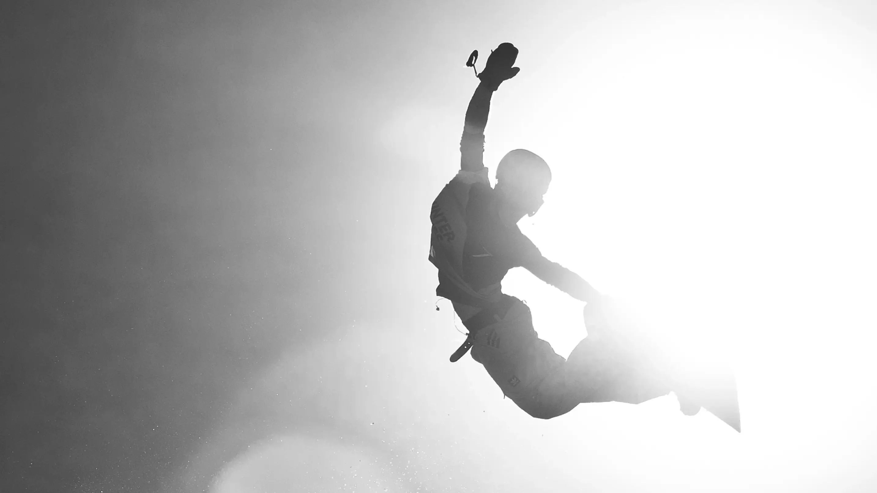 Silhouette of a snowboarder mid-air performing a grab trick against a bright sunlit sky, showcasing dynamic movement and freestyle energy.