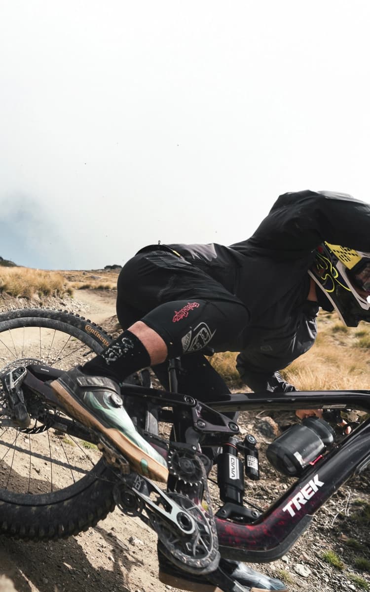 A mountain biker carving through a dirt berm at speed, leaning low as gravel sprays from the rear tire.